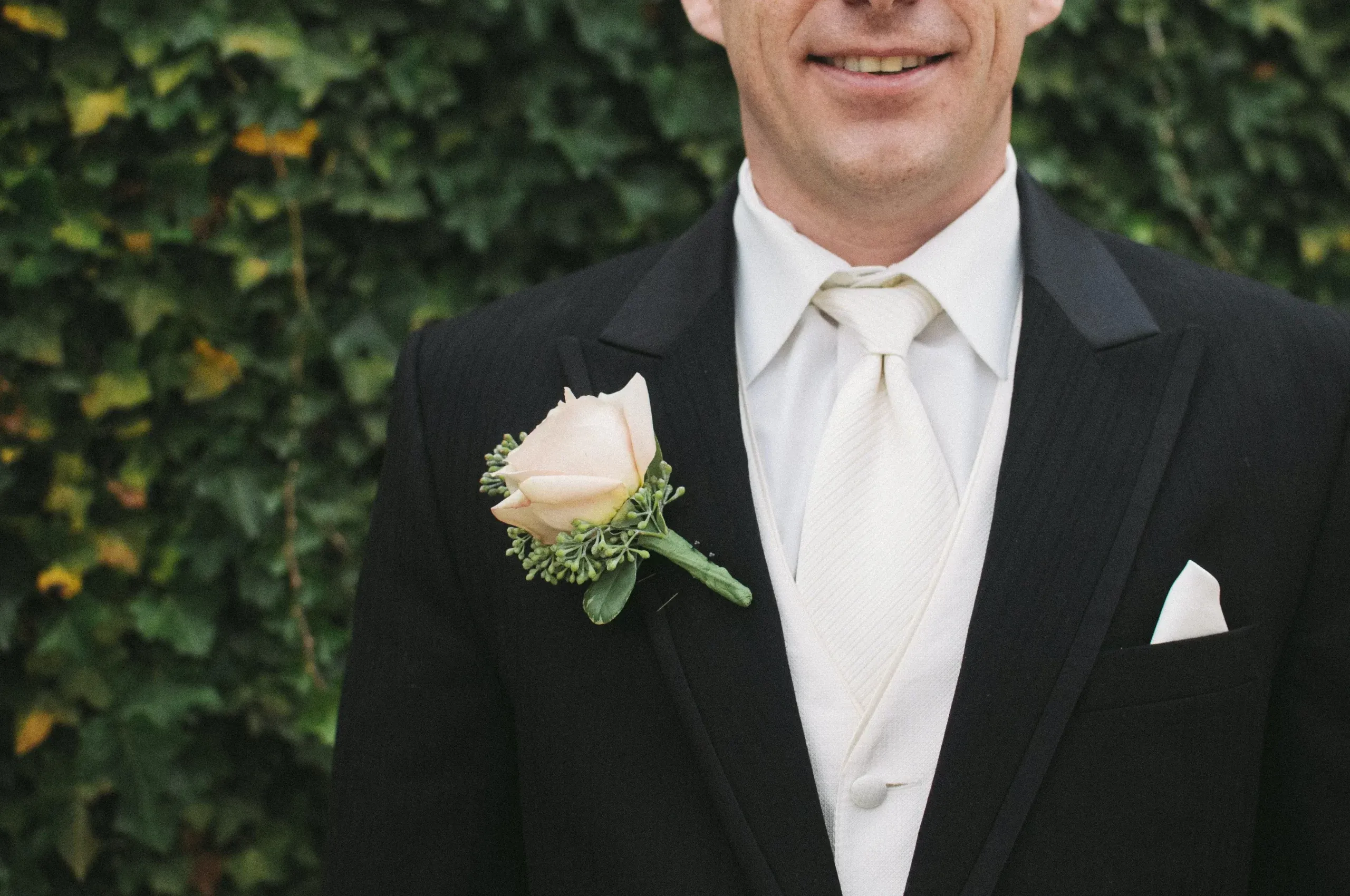 a best man in a black suit and white shirt and white tie, smiles warmly as he waits nervously to make his speech