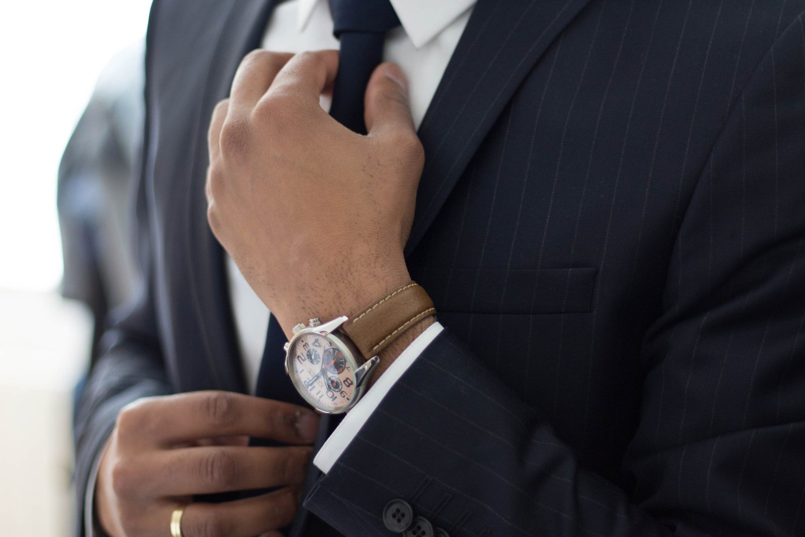 A best man in a dark suit with a very fancy watch, adjusts his tie